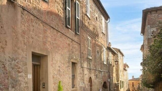 Een smalle straat met stenen tegels, begrensd door historische gebouwen met ronde deuropeningen en luiken.