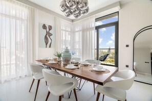 A dining area with a long wooden table, white chairs, and a large window with a view of the city. - Luxury Penthouse Retreat - Private Beach, Breathtaking Palm and Marina Views (Dubai Marina)