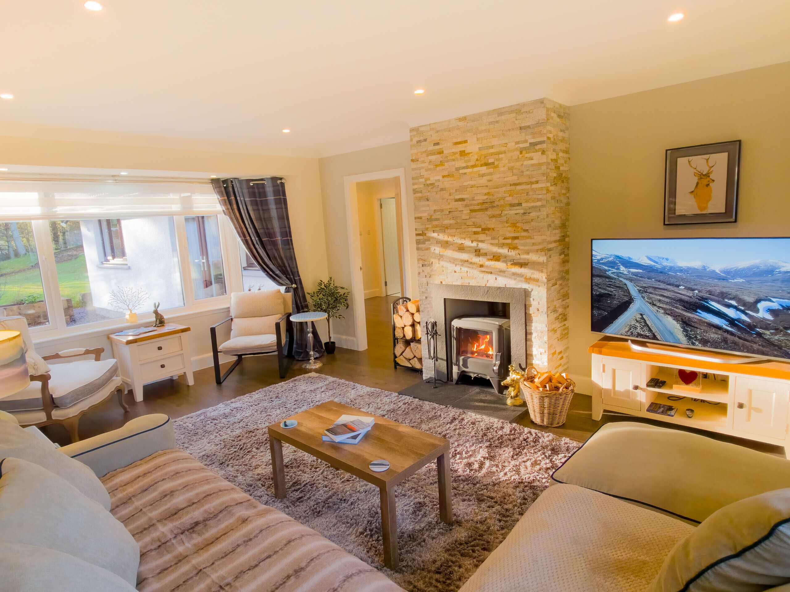 A wide shot of the comfortable living area, featuring soft sofas, cushions, and a warming fireplace, perfect for relaxing after a day in the Cairngorms.