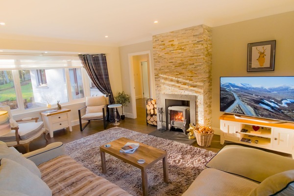 A wide shot of the comfortable living area, featuring soft sofas, cushions, and a warming fireplace, perfect for relaxing after a day in the Cairngorms.