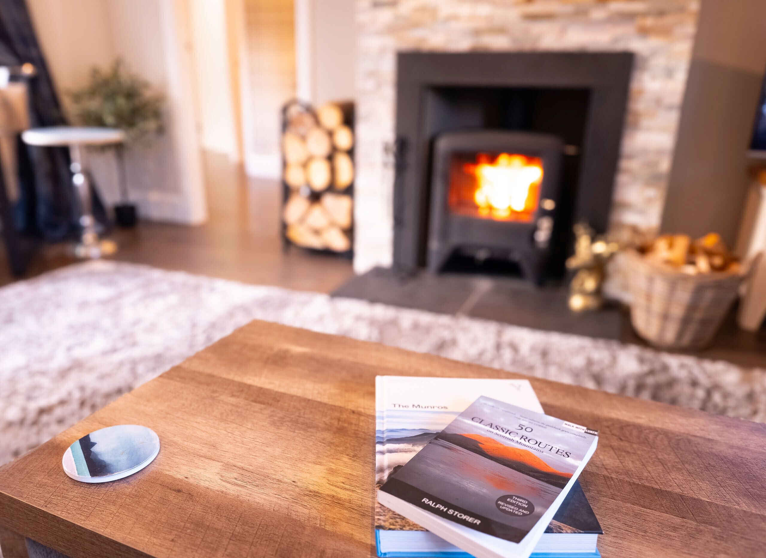 A cozy living room with a fireplace, a wooden coffee table, and a book titled "50 Classic Routes".