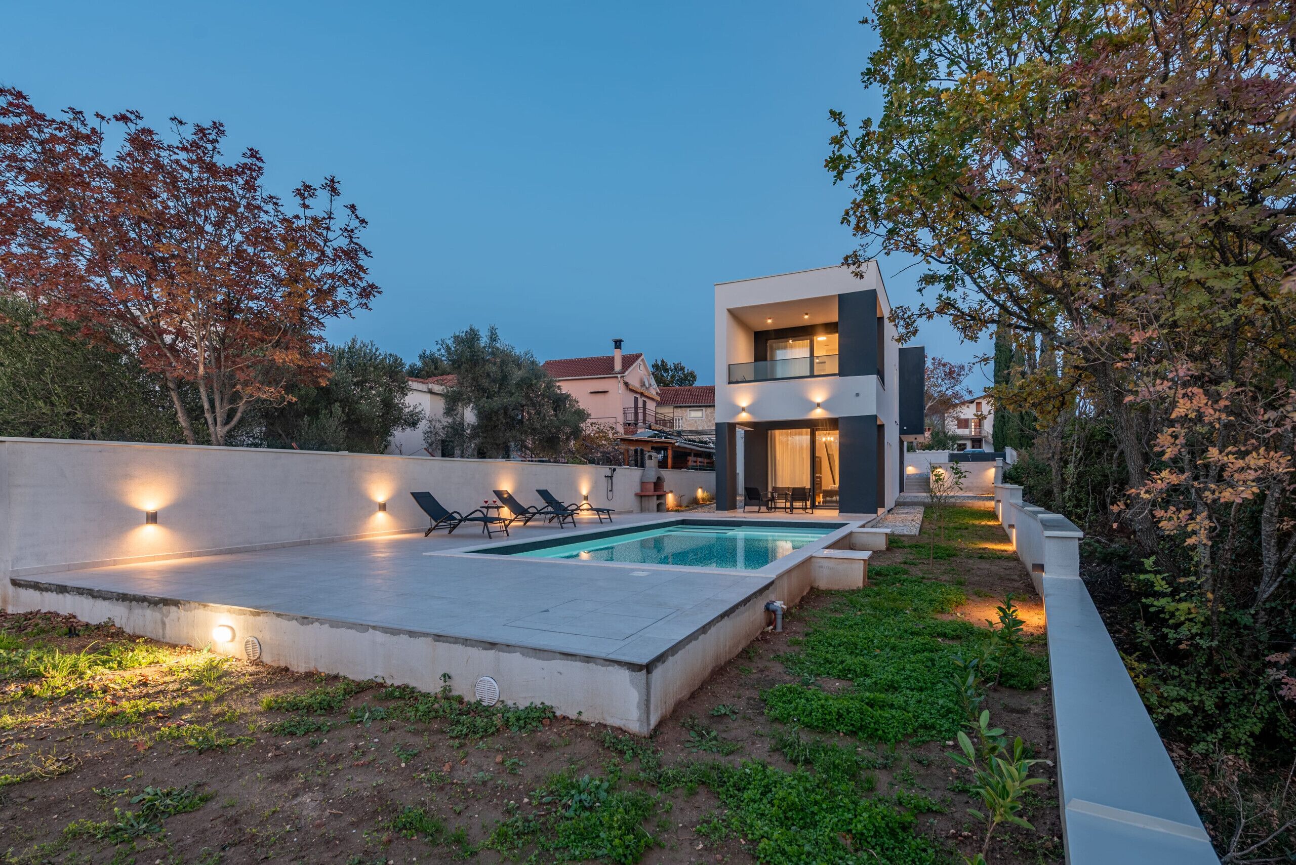 Une maison moderne dotée d’une piscine, d’un espace extérieur aménagé et d’un jardin bien éclairé.
