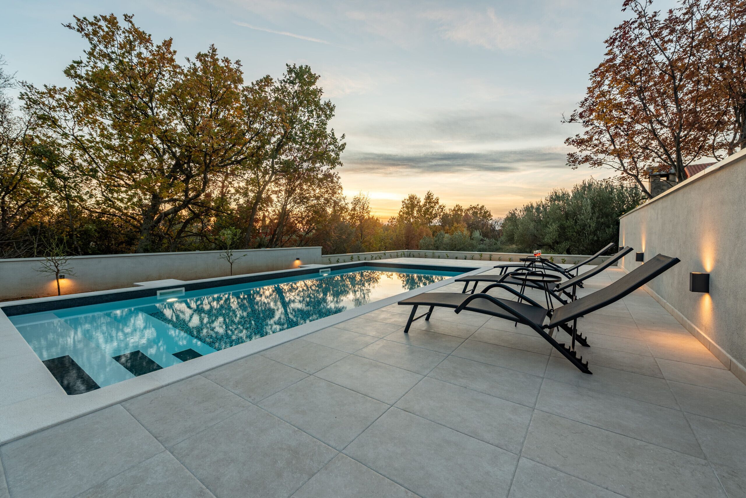 A swimming pool with lounge chairs and a sunset view.