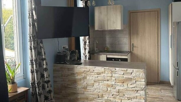 Une cuisine moderne dotée d’un îlot central, d’appareils électroménagers intégrés et d’une fenêtre agrémentée de rideaux à motifs.