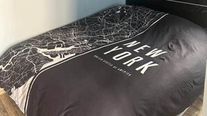 Un lit simple avec une couvre-lit à motifs noir et blanc et un oreiller orné du mot « NEW YORK ».