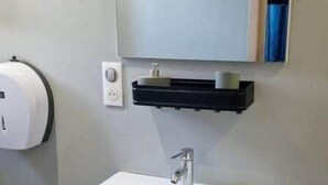 Une salle de bain avec un lavabo blanc, un miroir au-dessus et un distributeur de savon fixé au mur.