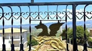 A wrought iron gate with a golden lion emblem, set against a backdrop of a clear sky and distant landscape.