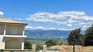 Un edificio con techo de tejas, pared de piedra y vista a montañas y un cielo despejado.