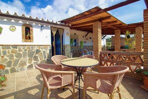 Une terrasse extérieure avec des meubles en osier, un mur en pierre et une pergola en bois.