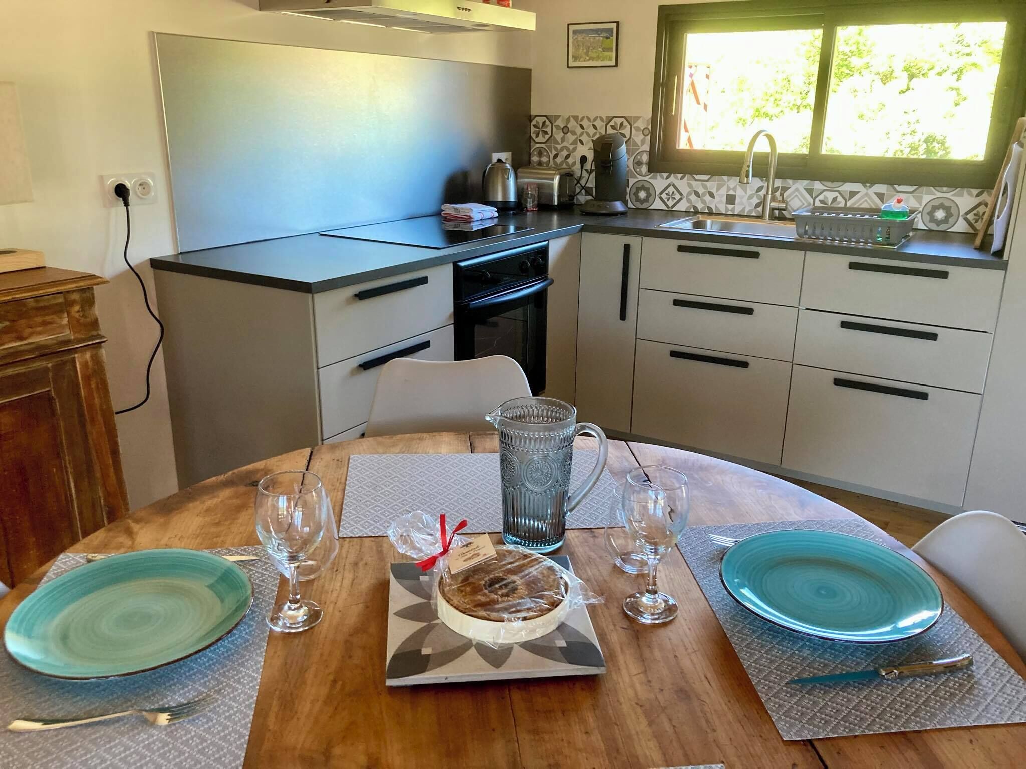 A compact kitchen with a dining area. It includes a stove, sink, and a window with a view of greenery.