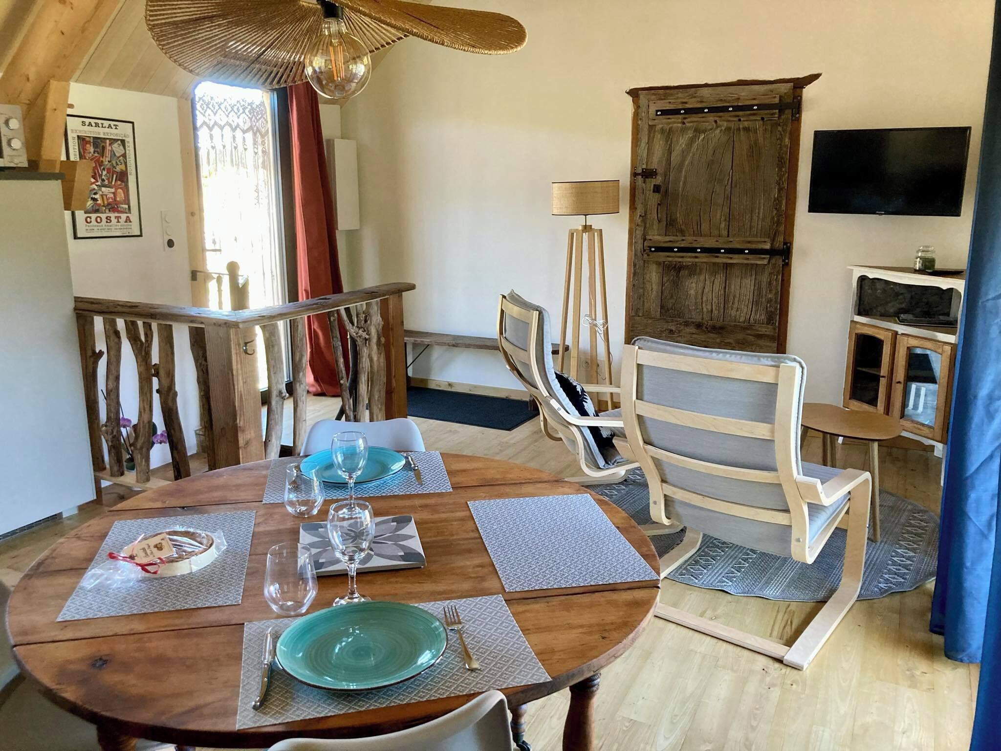 A dining area with a wooden table set for two, a wooden chair, a hanging light fixture, and a rustic wooden cabinet.
