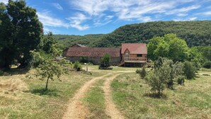 A rustic barn-style building with a dirt path leading to it, surrounded by trees and hills. - Le PERCHOIR, comfortable gîte (Bouzic)