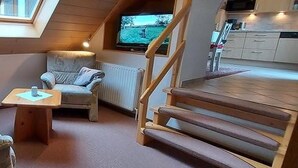 A loft-style room with a wooden staircase, a sofa, a table, and a television. - Apartment 4 with Balcony and Wi-Fi (Horumersiel)