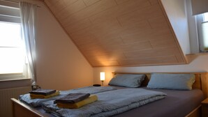 A bedroom with two beds, a sloped ceiling, a bedside table with a lamp, and a window with curtains. - Apartment 'Ferienwohnung 3' with Balcony and Wi-Fi (Horumersiel)