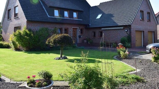 A two-story house with a sloped roof, brick exterior, and a well-maintained lawn with a small tree and flower beds. - Apartment 'Ferienwohnung 3' with Balcony and Wi-Fi (Horumersiel)