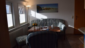 A dining area with a table set for two, a sofa, and a painting on the wall.