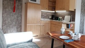 A compact kitchen with wooden cabinets, a microwave, a coffee maker, and a dining table with plates and cups.