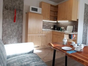 A compact kitchen with wooden cabinets, a microwave, a coffee maker, and a dining table with plates and cups.
