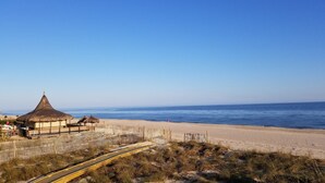 A beach with a wooden fence, a thatched-roof building, and a clear blue sky. - Island Suites - Beachfront, boutique hotel, walk to lighthouse, dining & more (St George Island)