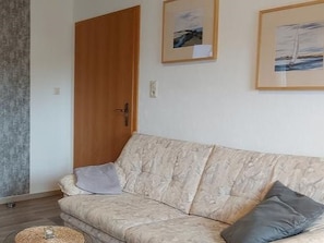 Un salon avec un canapé, une porte en bois et deux tableaux encadrés accrochés au mur.