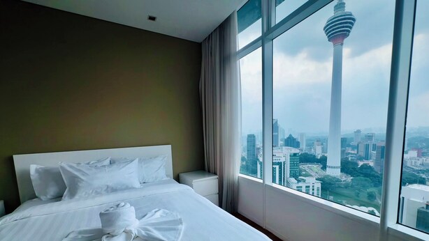 Una habitación de hotel con una cama grande, una cama bien tendida con una toalla, una mesita de noche y vistas a un paisaje urbano con una torre destacada.
