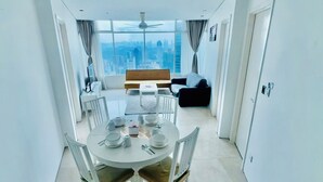 Un comedor moderno con una mesa redonda preparada para cuatro personas, paredes blancas y vistas a la ciudad a través de amplios ventanales.