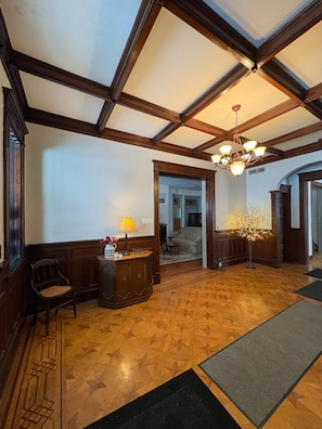 A lobby with a wooden floor, a reception desk, a chandelier, and a door leading to another room.