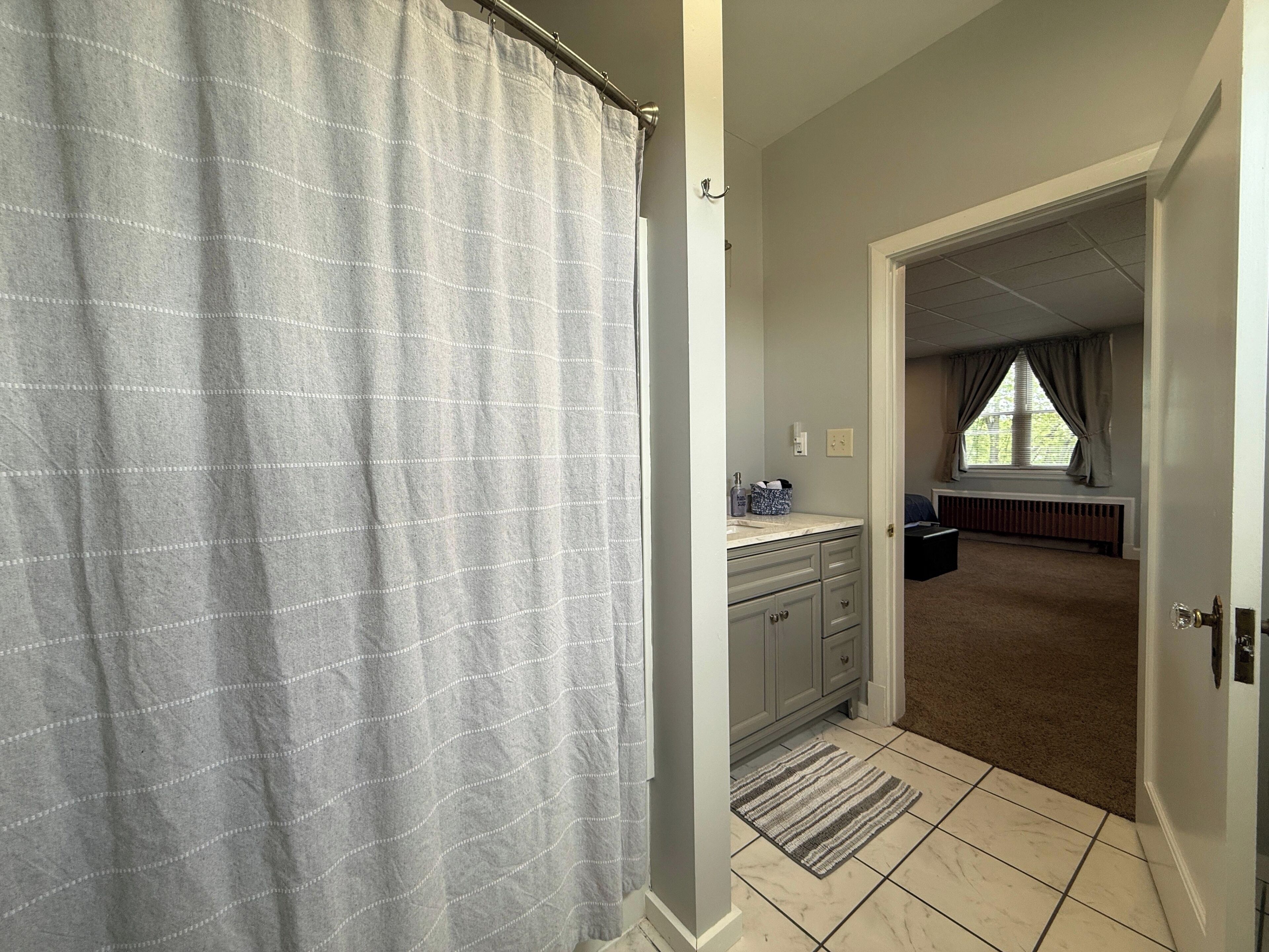 A bathroom with a shower curtain, a sink with a towel, and a radiator.