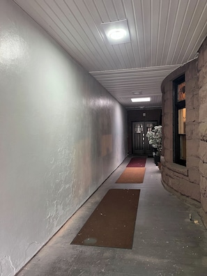 A corridor with a stone wall, a door at the end, and a red mat on the floor.