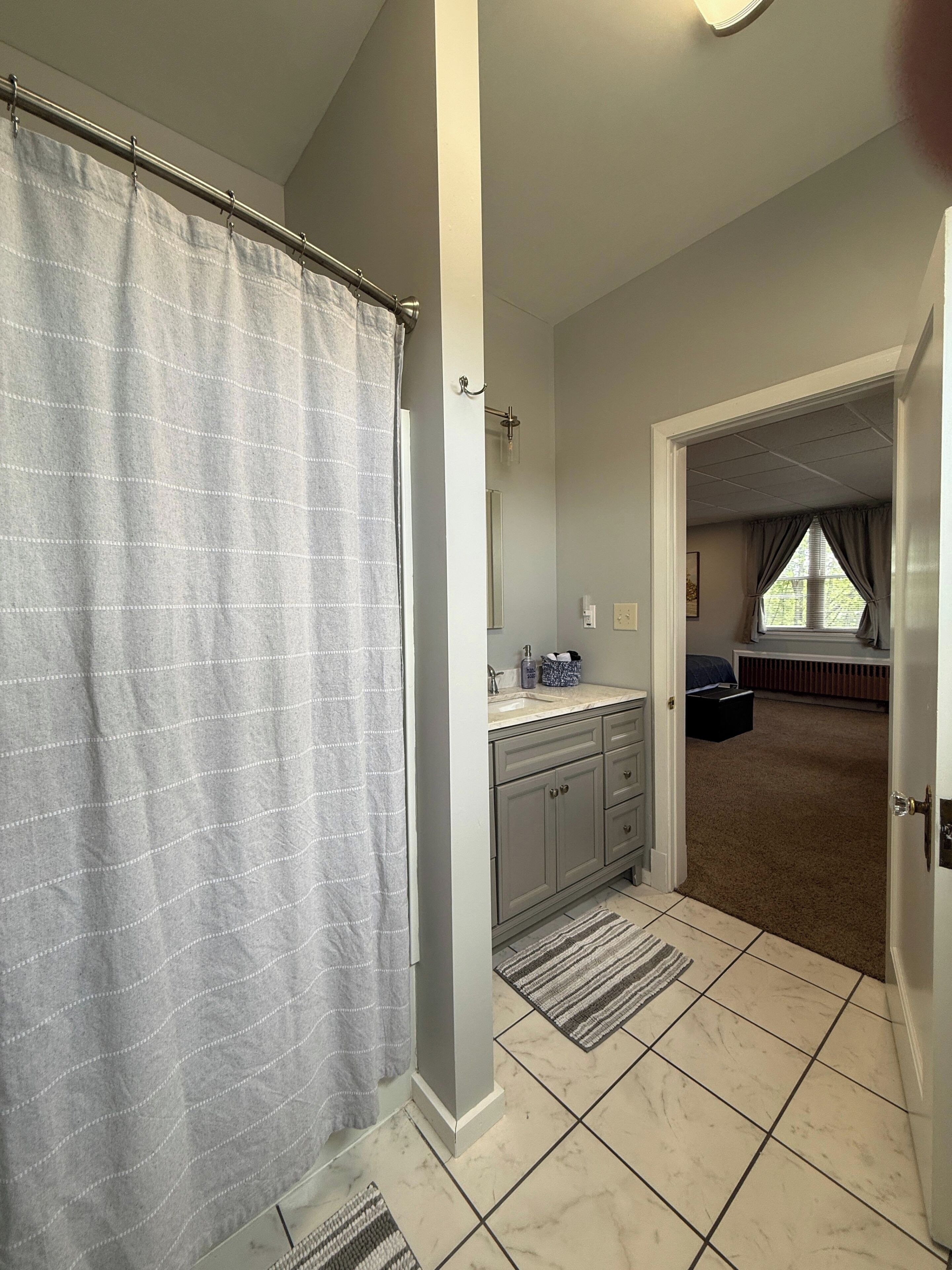 A bathroom with a shower curtain, a sink, and a mirror.
