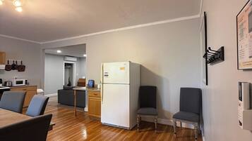 Una cocina moderna con refrigerador, piso de madera y un área de comedor con sillas.