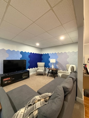 A living room with a TV, sofa, armchair, and a wall with hexagonal patterns. - NH4:Timeless Elegance 1BR Haven in Historic Home (DuBois)
