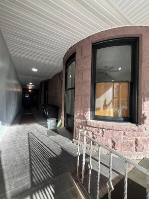 A corridor with a curved stone wall, a window with blinds, a metal railing, and a ceiling with linear lights.