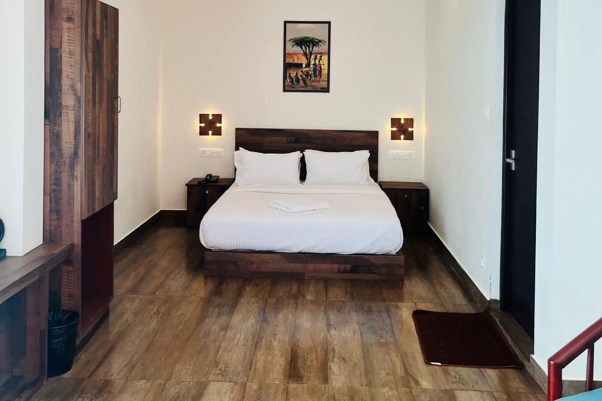 A bedroom with a large bed, wooden flooring, a ceiling fan, and a painting on the wall.
