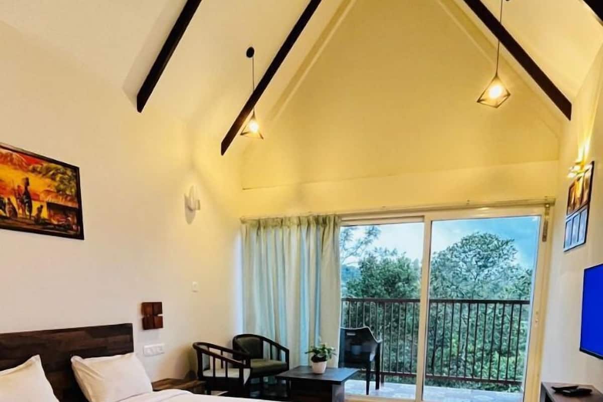A bedroom with a large bed, a desk, a chair, and a balcony with a view of trees.