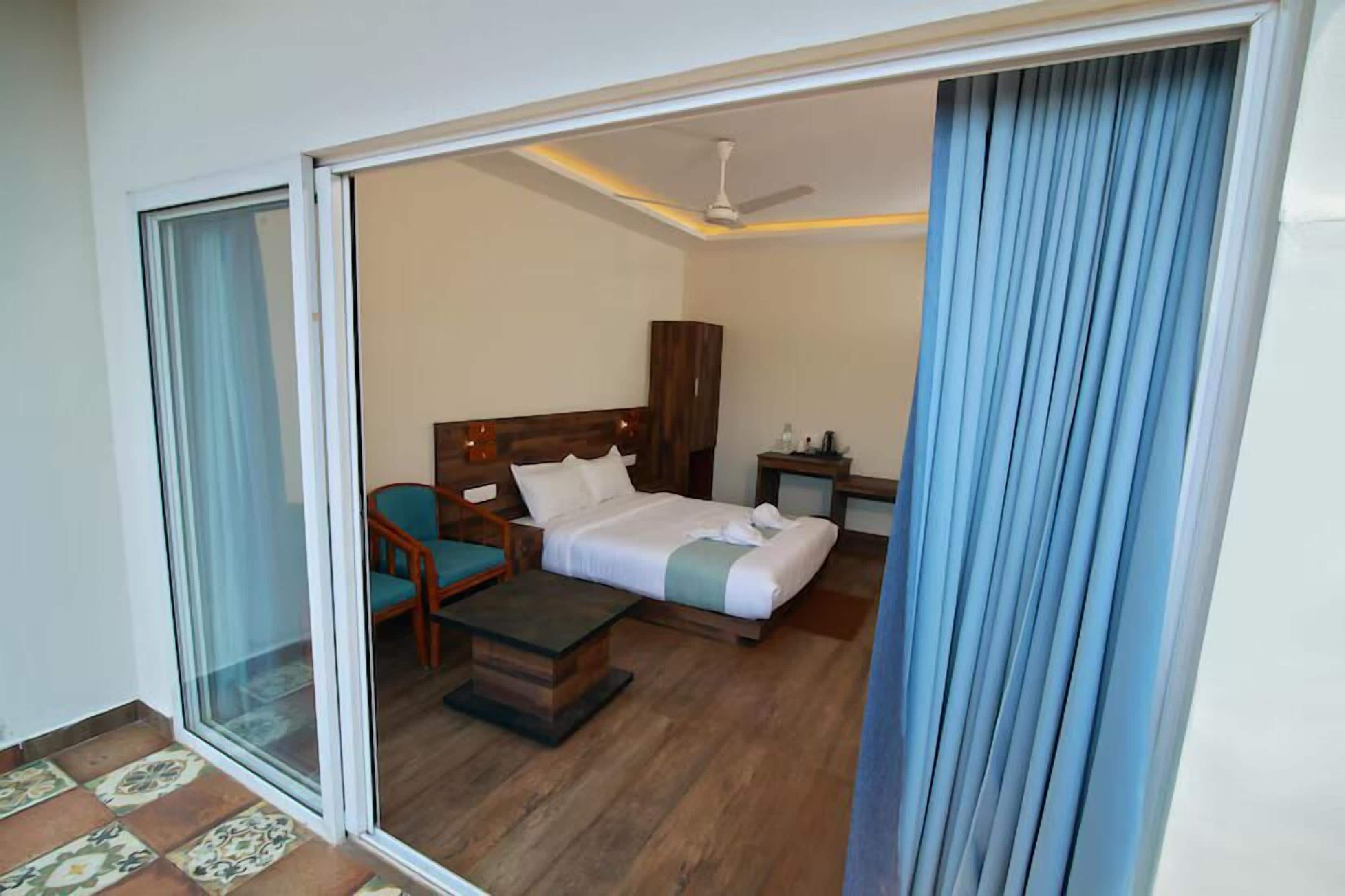 A hotel room with a bed, a chair, a small table, a nightstand, and a ceiling fan.