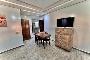 Ein Essbereich mit Holztisch und Stühlen, einem Holzschrank und einem an der Wand befestigten Fernseher.