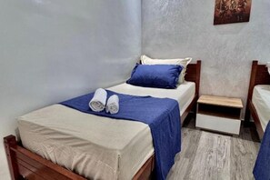 Ein kleiner, ordentlicher Raum mit einem Bett, einem Nachttisch und einem an der Wand befestigten Regal.
