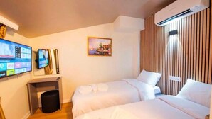 Ett hotellrum med två sängar, en tv som är monterad på väggen, en luftkonditioneringsanläggning och en tavla på väggen.