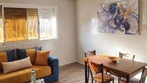 A modern living room with a sofa, dining table, and chairs. There is a window with blinds and a painting on the wall. - Bonne étoile Imsouane : ground floor Apartment (Imsouane,)