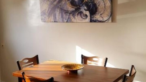 A dining area with a wooden table and chairs, a decorative bowl on the table, and a large abstract painting on the wall. - Bonne étoile Imsouane : ground floor Apartment (Imsouane,)