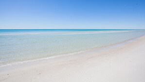 Ampia spiaggia sabbiosa con acqua cristallina e cielo sereno.