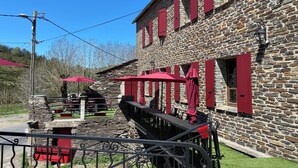 Ein Steinhaus mit roten Fensterläden und Außenbestuhlung mit roten Sonnenschirmen.