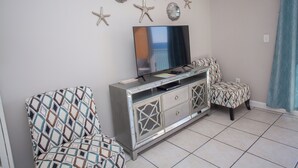 Ein Wohnzimmer mit Fernseher auf einer Spiegelwand, gemusterten Sesseln und Wanddekoration mit Meeressternen.