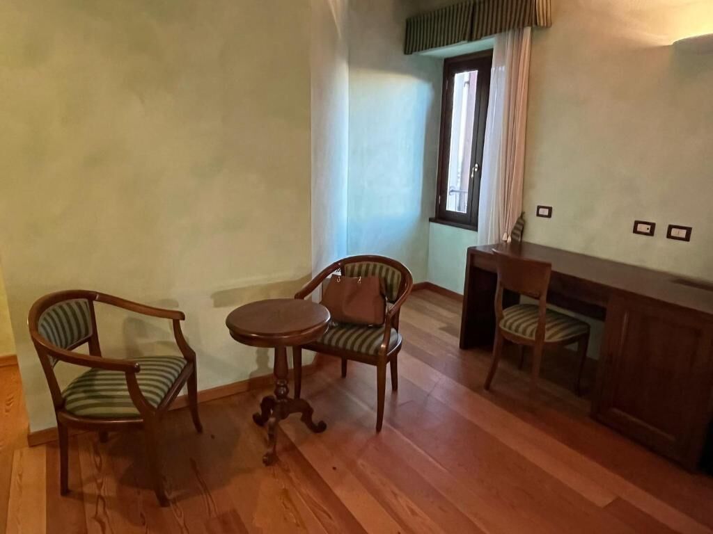 A room with wooden flooring, a round table with chairs, a small cabinet, and a window with curtains.
