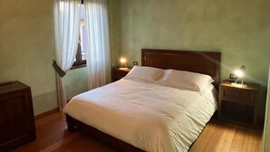 Un dormitorio con cama de madera, dos mesitas de noche con lámparas, una ventana con cortinas y suelo de madera.