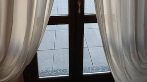 Vista a través de una ventana con cortinas translúcidas, piso de baldosas y baranda de metal en el exterior.