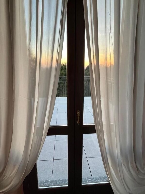 A view through a window with sheer curtains, a tiled floor, and a metal railing outside.