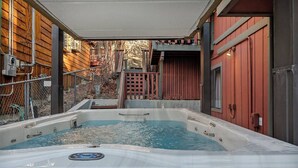A hot tub in a covered outdoor area with wooden walls and a red building in the background. - Wildwood Chalet, 5 mins to ski resorts w/game room (Big Bear Lake)