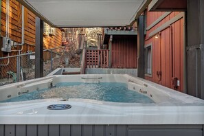 Un bain à remous situé dans un espace extérieur abrité, avec des murs en bois et un bâtiment rouge en arrière-plan.